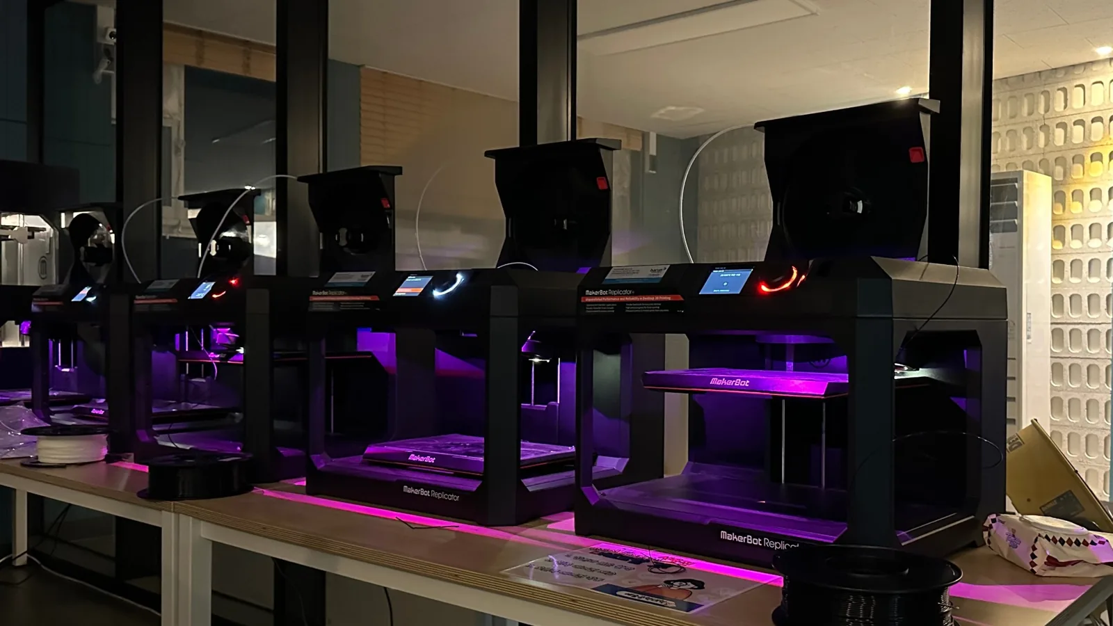 보라색 조명이 켜진 3D 프린터 다섯 대가 나란히 돌아가고 있다.